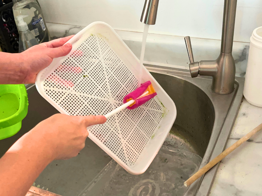 a person holding a sponge and a basket under running water