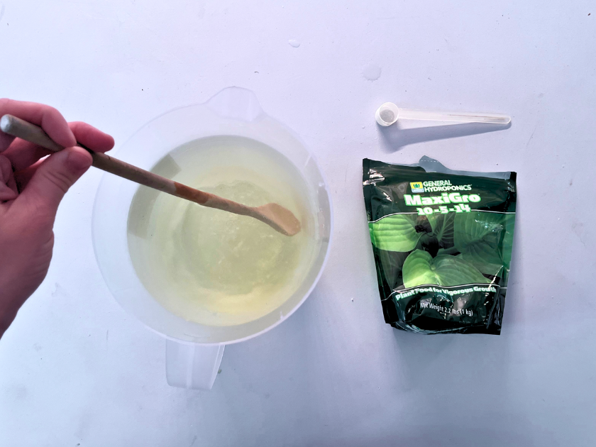 a hand holding a wooden spoon in a clear container with liquid